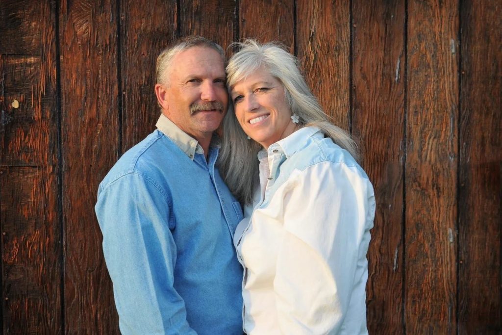 Ron and Sue, owners of this rustic North Idaho Wedding Venue, posing by their barn wall.
